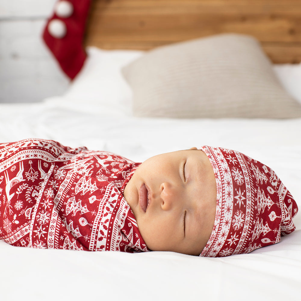 Alternative close up image of a child swaddled on a bed in a Reindeer Cheer swaddle and hat set