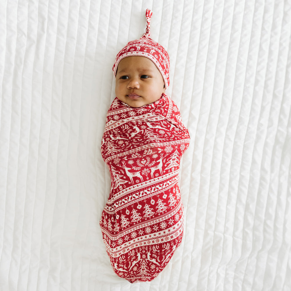 Child swaddled on a bed in a Reindeer Cheer swaddle and hat set