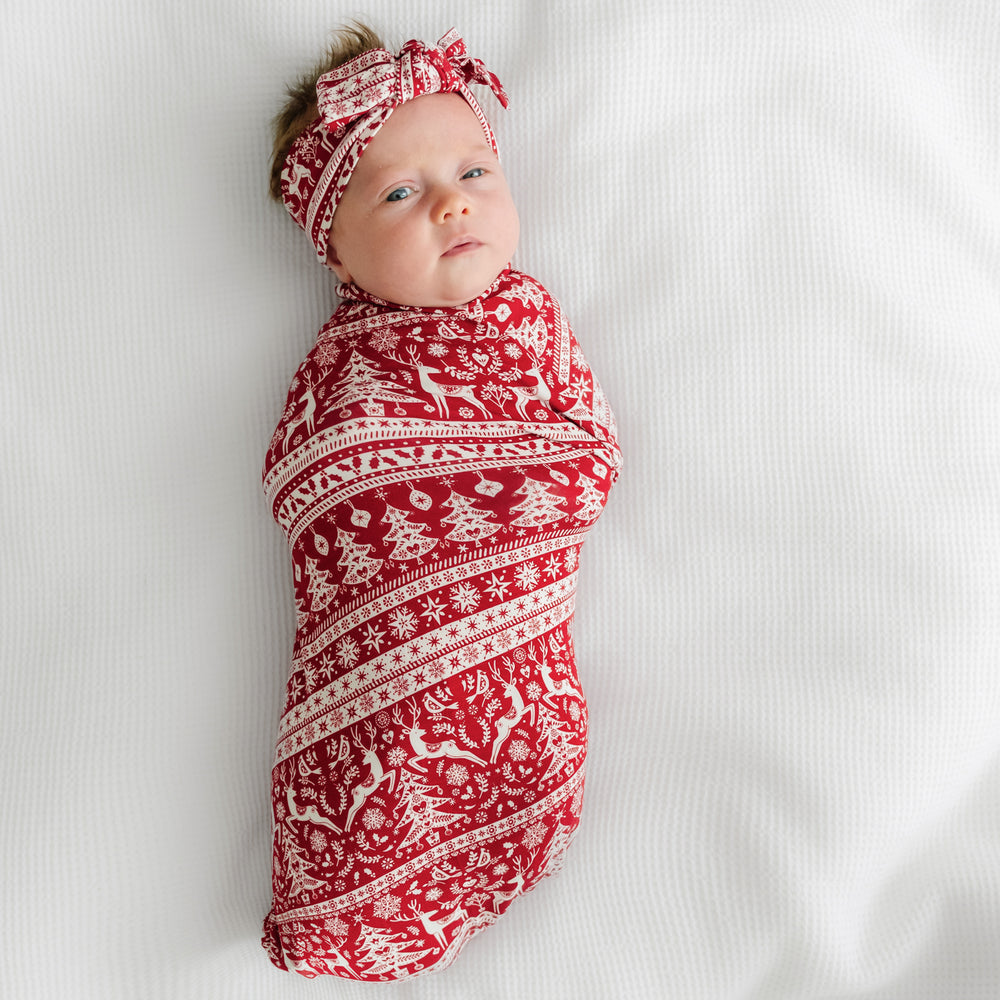 Child swaddled on a bed in a Reindeer Cheer swaddle and headband set