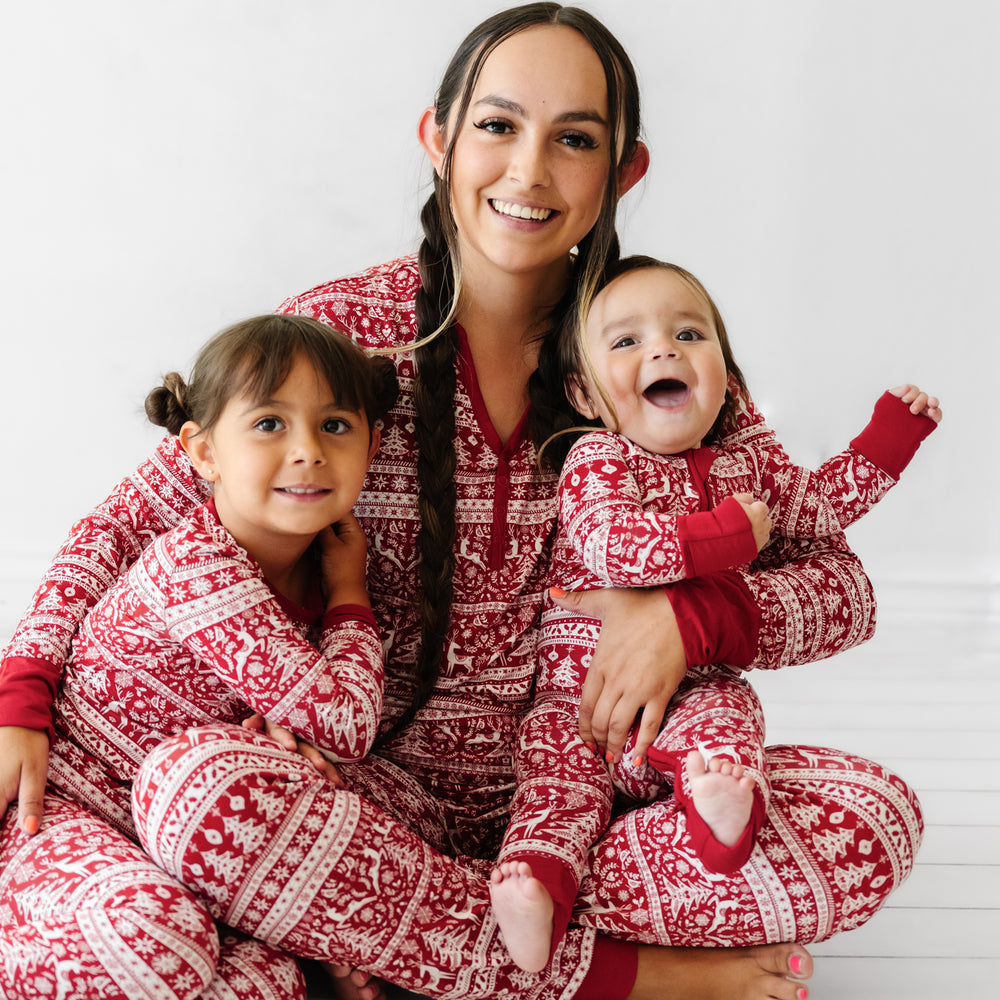 Mother and her two children sitting together. Mom is wearing Reindeer Cheer women's pajama top and matching bottoms. Children are wearing Reindeer Cheer two piece and zippy pajamas 