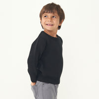 Side view image of a child wearing a Black knit sweater