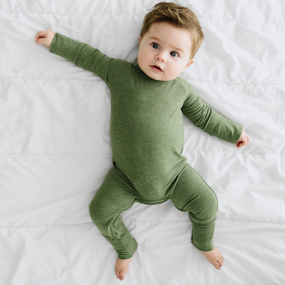 Child laying on a blanket wearing a Heather Cypress Green Ribbed Crescent Zippy