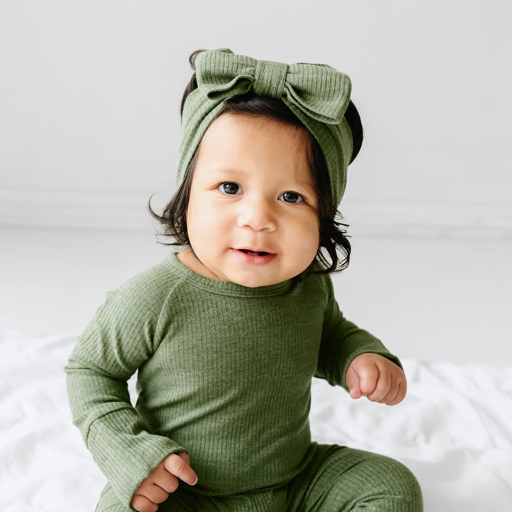 Child wearing a Heather Cypress Green Ribbed luxe bow headband and matching crescent zippy