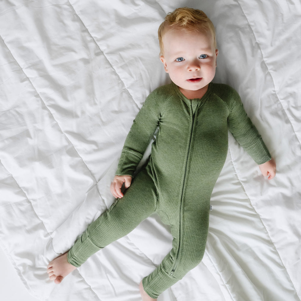 Child laying on a blanket wearing a Heather Cypress Green Ribbed zippy