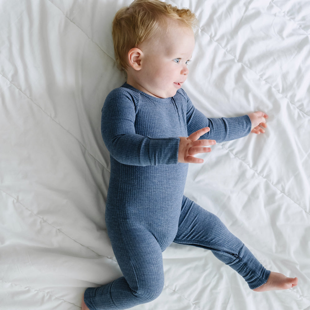 Side view image of a child laying on a blanket wearing a Heather Dusty Indigo Ribbed crescent zippy