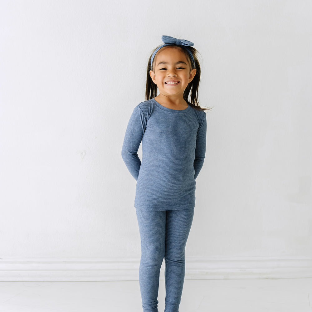 Child wearing a Heather Dusty Indigo ribbed two piece pajama set paired with a matching luxe bow headband set