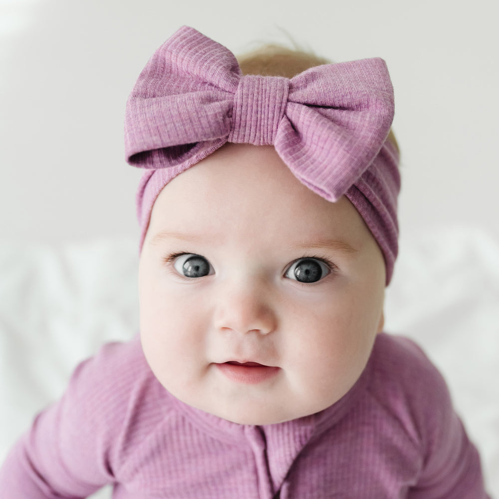 Close up image of a child wearing a Heather Mulberry ribbed luxe bow headband paired with a matching zippy