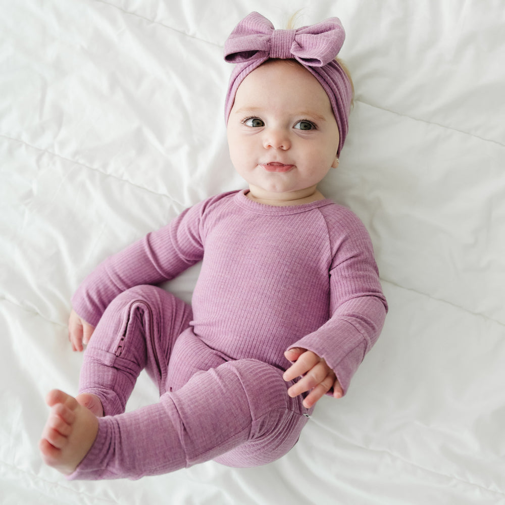 Image of a child wearing a Heather Mulberry ribbed luxe bow headband paired with a matching crescent zippy