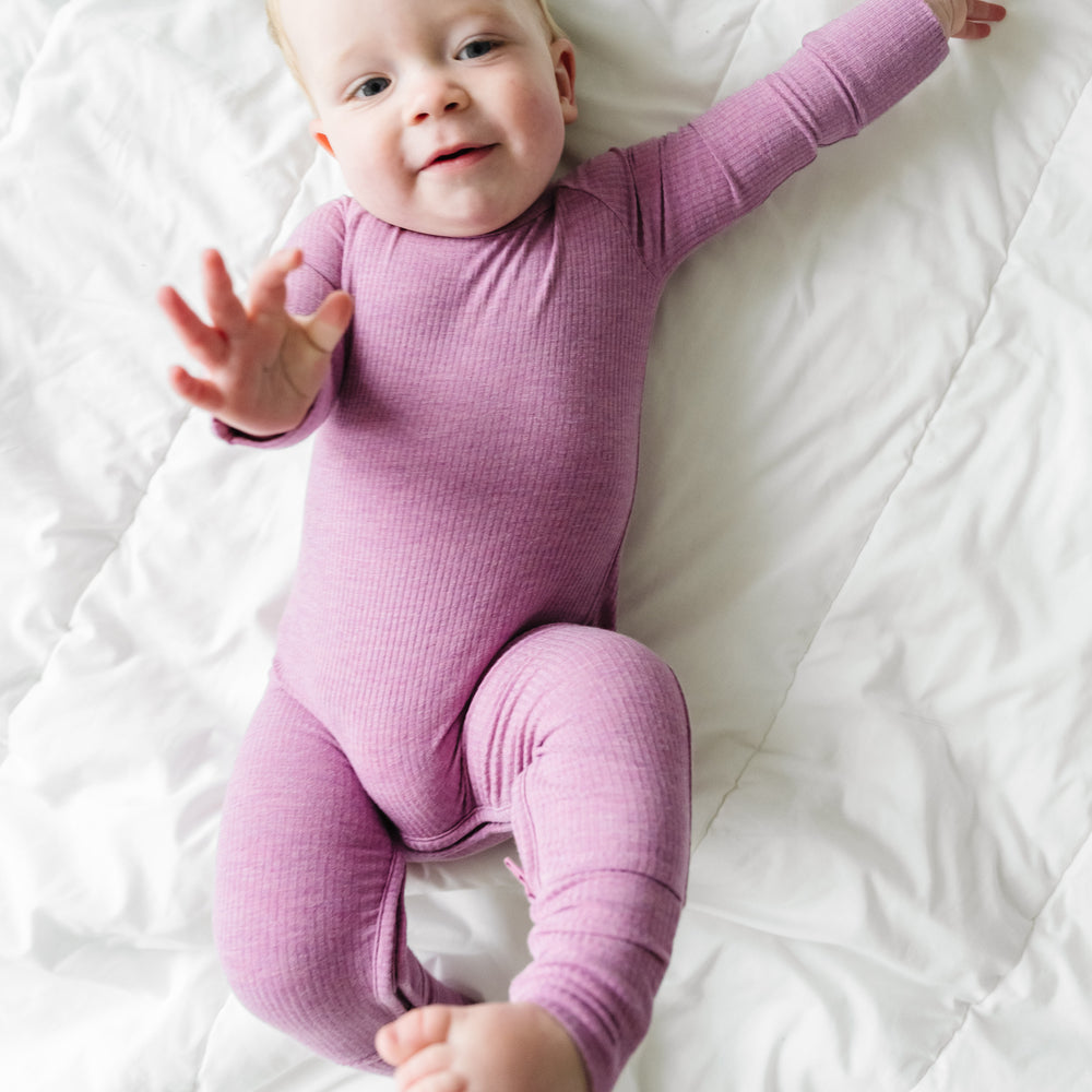 Child laying on a blanket wearing a Heather Mulberry Ribbed Crescent Zippy