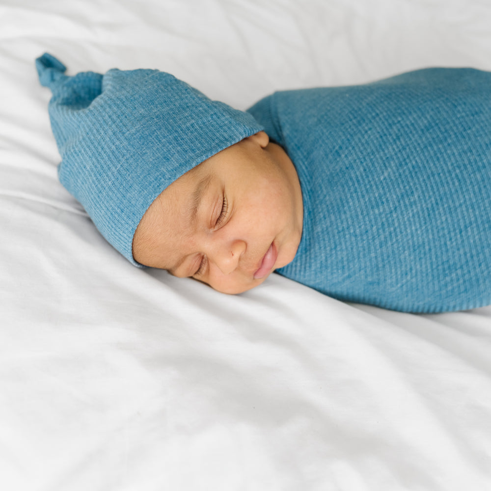 Close up image of child swaddled in a Heather Blue Ribbed swaddle and hat set