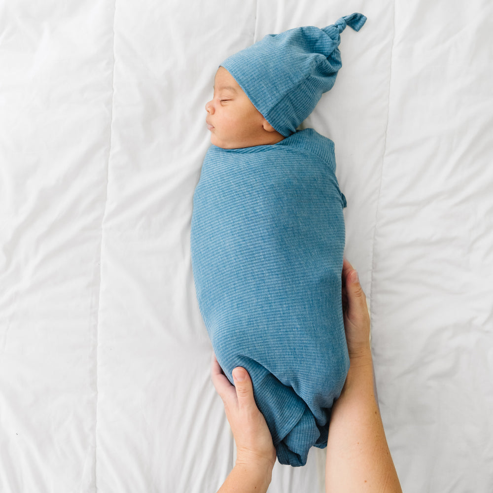 Mother swaddling her child in a Heather Blue Ribbed swaddle and hat set