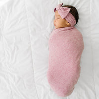 Child swaddled in a Heather Mauve Ribbed swaddle and luxe headband set
