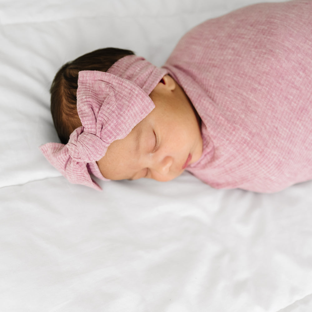 Close up image of a child swaddled in a Heather Mauve Ribbed swaddle and luxe headband set