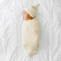 Child swaddled in a Heather Oatmeal Ribbed swaddle and hat set