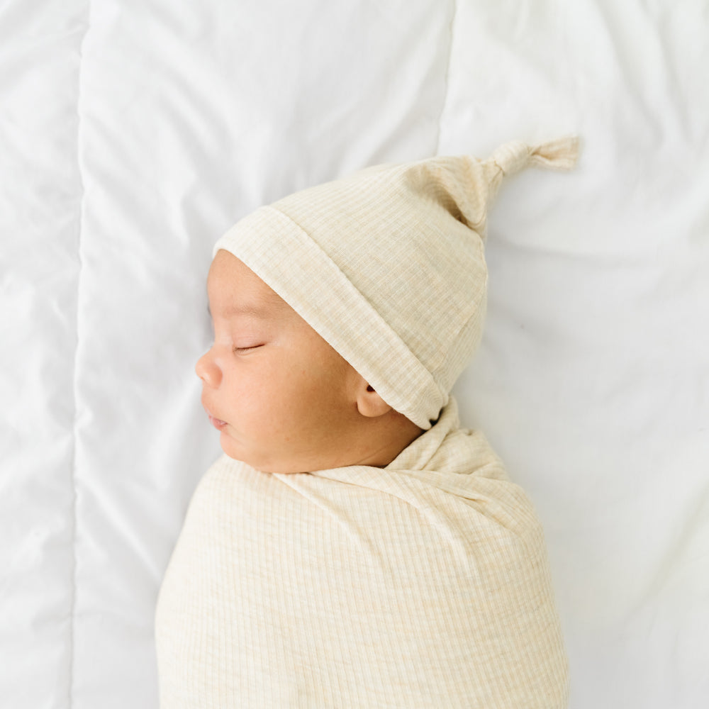 Close up image of a child swaddled in a Heather Oatmeal Ribbed swaddle and hat set