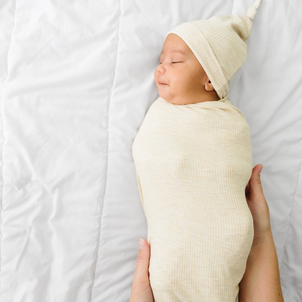 Mother swaddling her child in a Heather Oatmeal Ribbed swaddle and hat set