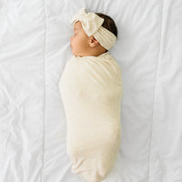 Child swaddled in a Heather Oatmeal Ribbed swaddle and luxe headband set