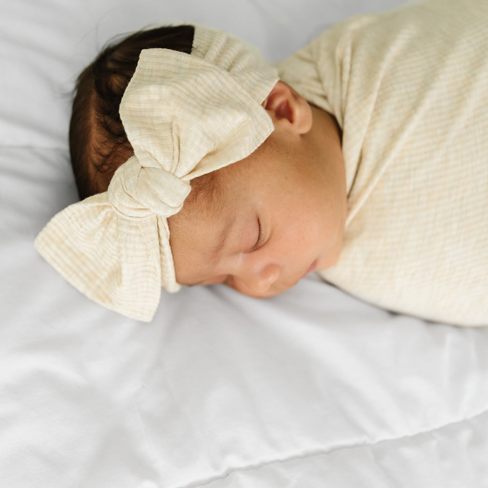 Close up image of child swaddled in a Heather Oatmeal Ribbed swaddle and luxe headband set