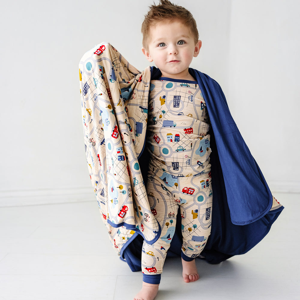 Click to see full screen - Child wearing a Blue Road Trip two piece pajama set holding up a matching large cloud blanket