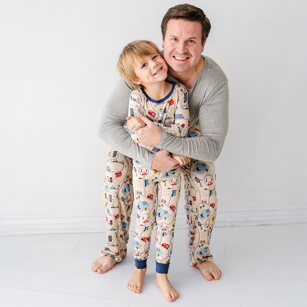 Click to see full screen - Father hugging his child wearing matching Road Trip pajamas. Dad is wearing men's Blue Road Trip pajama pants and solid Heather Gray men's pajama top. His child is wearing a Blue Road Trip two piece pajama set