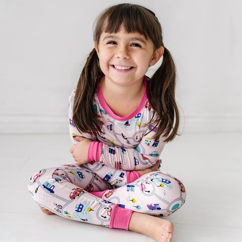Click to see full screen - Child sitting wearing a Rosy Road Trip two piece pajama set