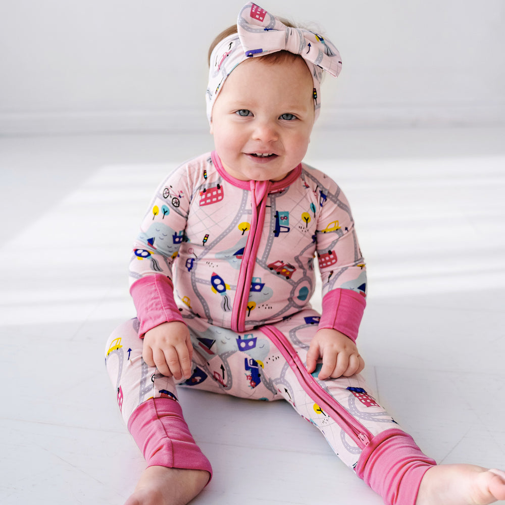 Child sitting wearing a Rosy Road Trip Zippy paired with a matching luxe bow headband