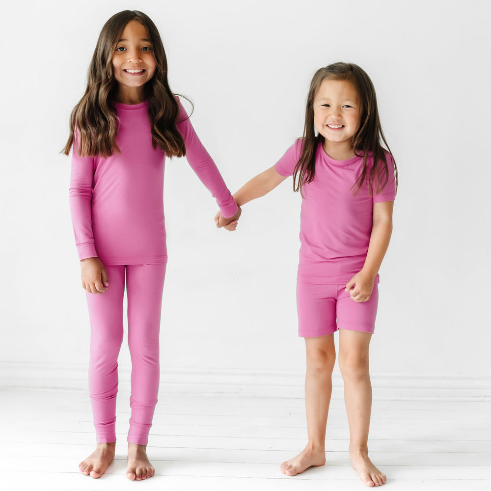 Two children holding hands wearing matching Rosette pajama sets. One child is wearing a Rosette two piece short sleeve and shorts pajama set and the other child is wearing a Rosette two piece pajama set in a long sleeve and pants style