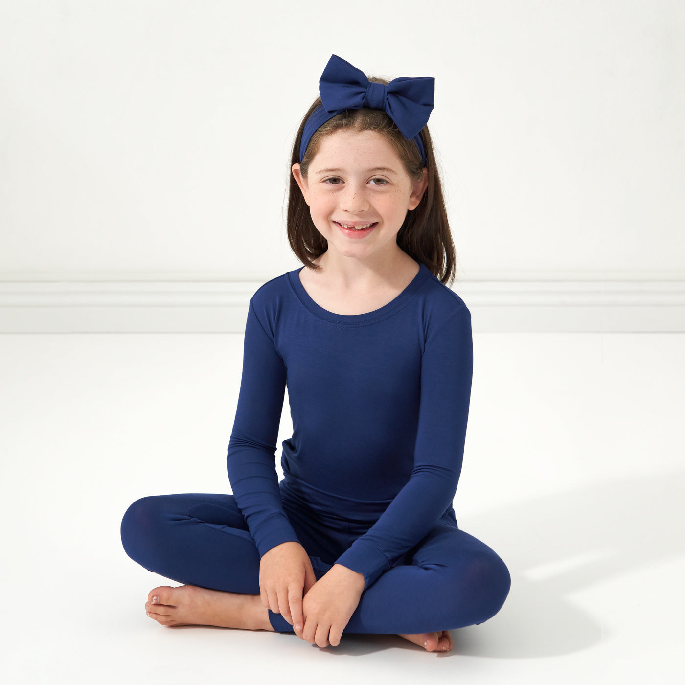 Child sitting wearing a Sapphire two piece pajama set paired with a matching luxe bow headband