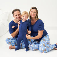 Family of three posing together wearing coordinating pajamas. Dad is wearing a men's Sapphire short sleeve pajama top paired with men's Hanukkah Lights and Love pajama pants. Mom is wearing women's Sapphire pajama top paired with women's Hanukkah Lights and Love pajama pants. Their child is coordinating wearing a Sapphire zippy