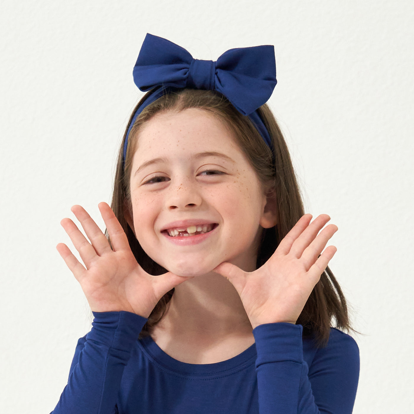 Close up image of a child wearing a Sapphire two piece pajama set paired with a matching Sapphire luxe bow headband