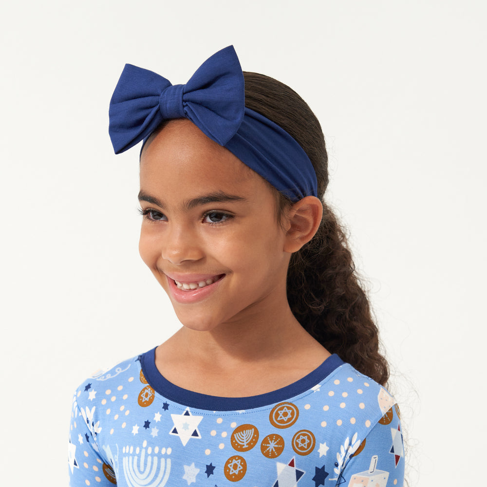 Close up image of a child wearing a Hanukkah Lights and Love two piece pajama set paired with a Sapphire luxe bow headband
