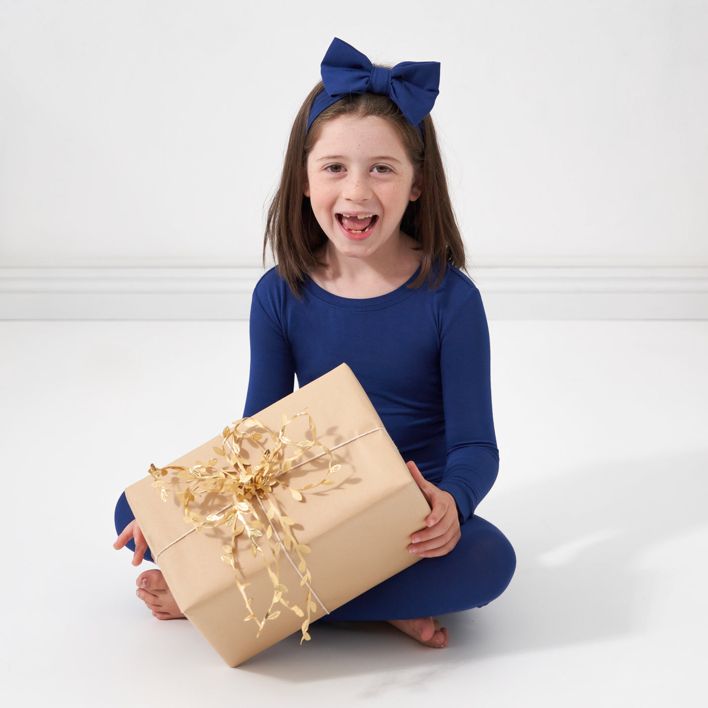 Child sitting wearing a Sapphire two piece pajama set paired with a matching Sapphire luxe bow headband