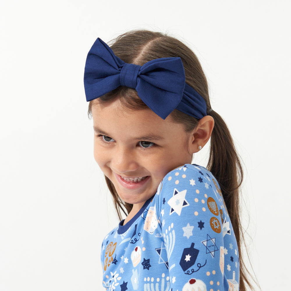 Child posing wearing a Hanukkah Lights and Love two piece pajama set paired with a Sapphire luxe bow headband