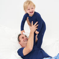 Father holding up his child wearing matching Sapphire pajamas. Dad is wearing a men's Sapphire short sleeve pajama top and child is wearing a Sapphire zippy