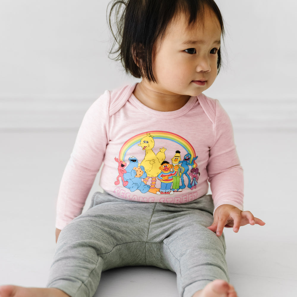 Child sitting on the ground wearing a Sesame Street pink graphic bodysuit