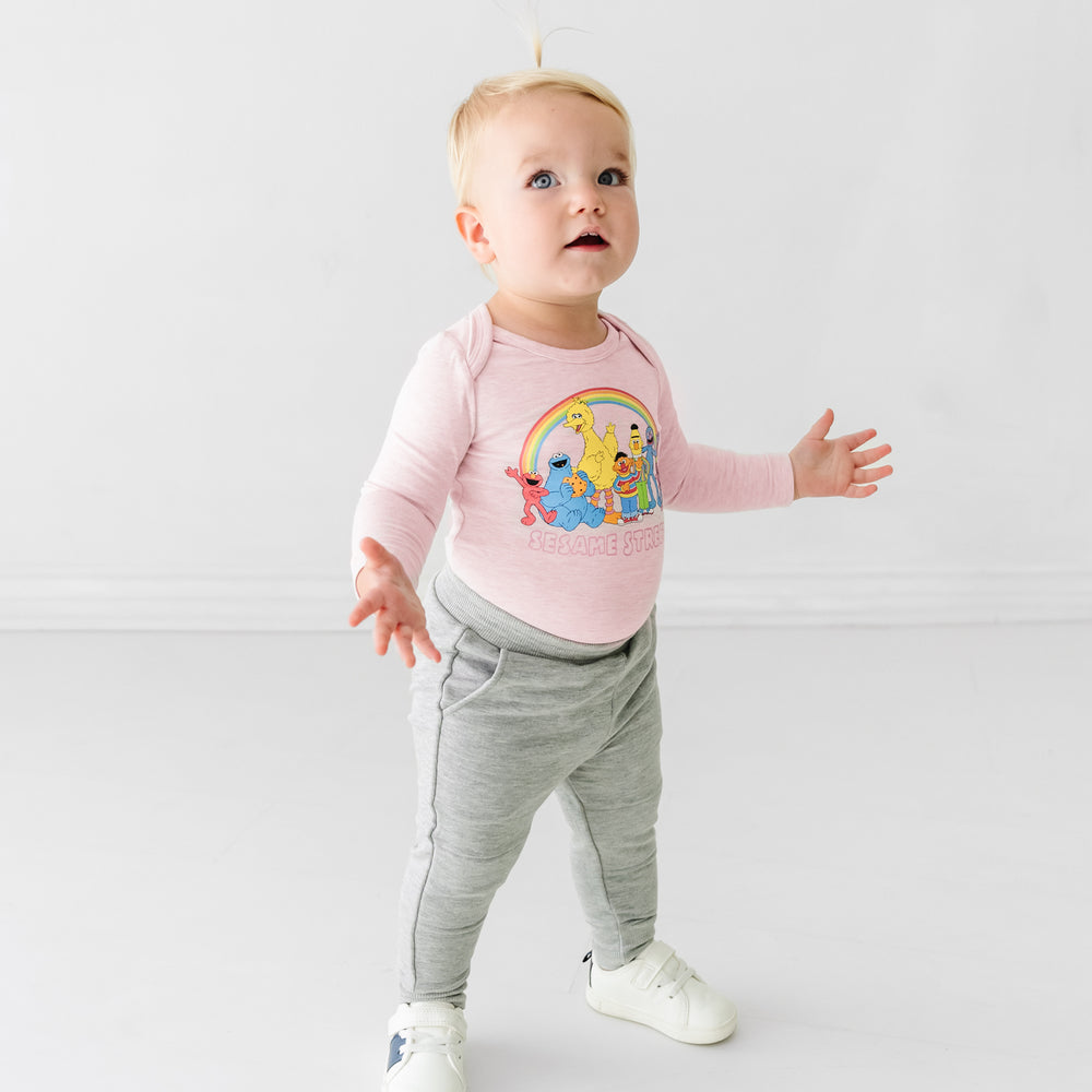 Child with their arms spread out wearing a Sesame Street pink graphic bodysuit
