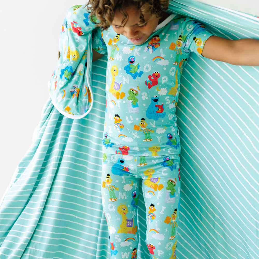 Close up image of a child holding a Spelling with Sesame Street large cloud blanket showing the striped backing