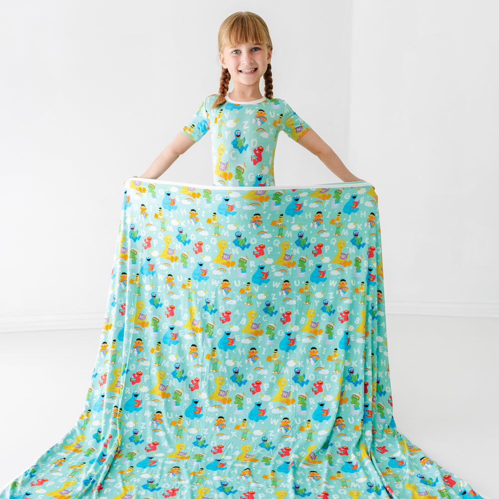 Child holding a Spelling with Sesame Street large cloud blanket in front of them