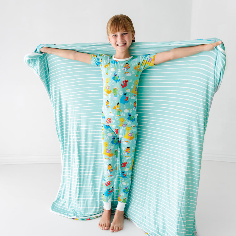 Child holding a Spelling with Sesame Street large cloud blanket showing the striped backing