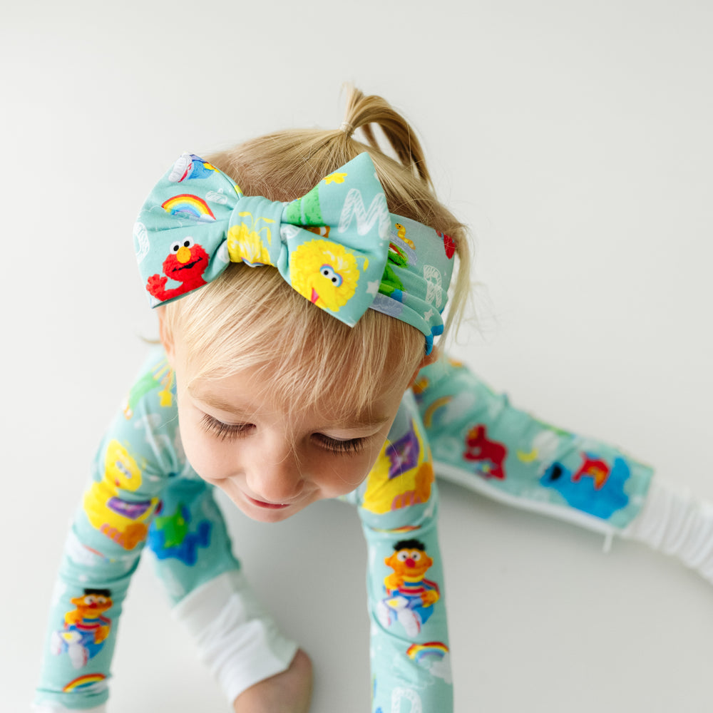 Close up image of a child sitting on the ground wearing a Spelling with Sesame Street luxe bow headband