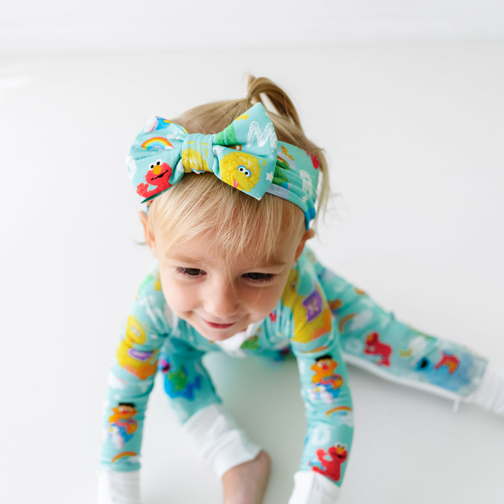 Child sitting on the ground wearing a Spelling with Sesame Street luxe bow headband