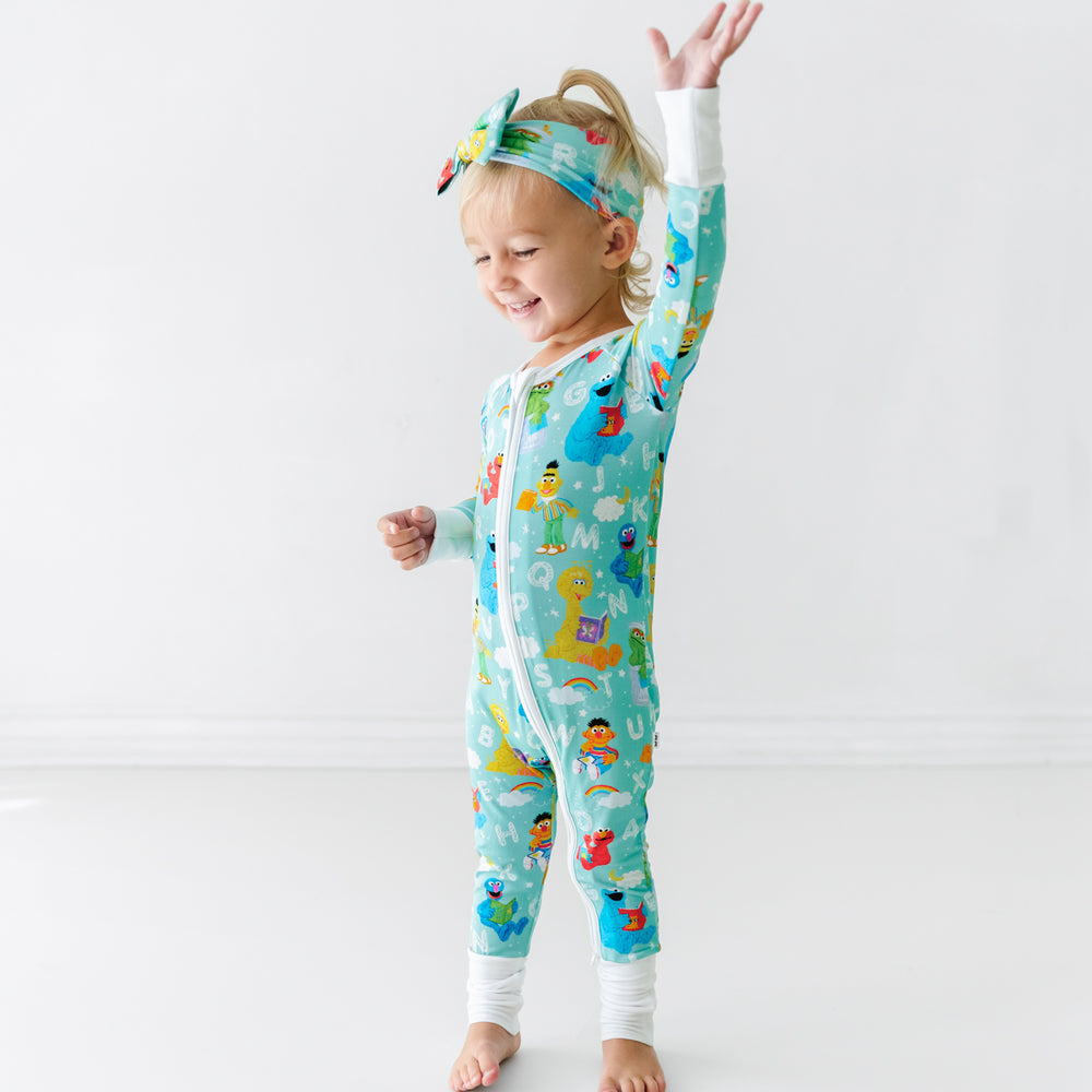 Child with her hand in the air wearing a Spelling with Sesame Street luxe bow headband and matching zippy