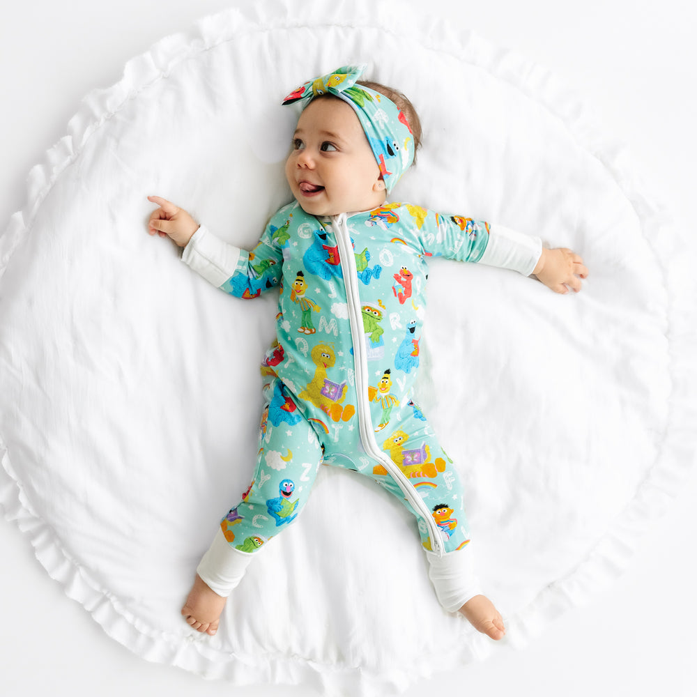 Child laying on a blanket wearing a Spelling with Sesame Street luxe bow headband and matching zippy