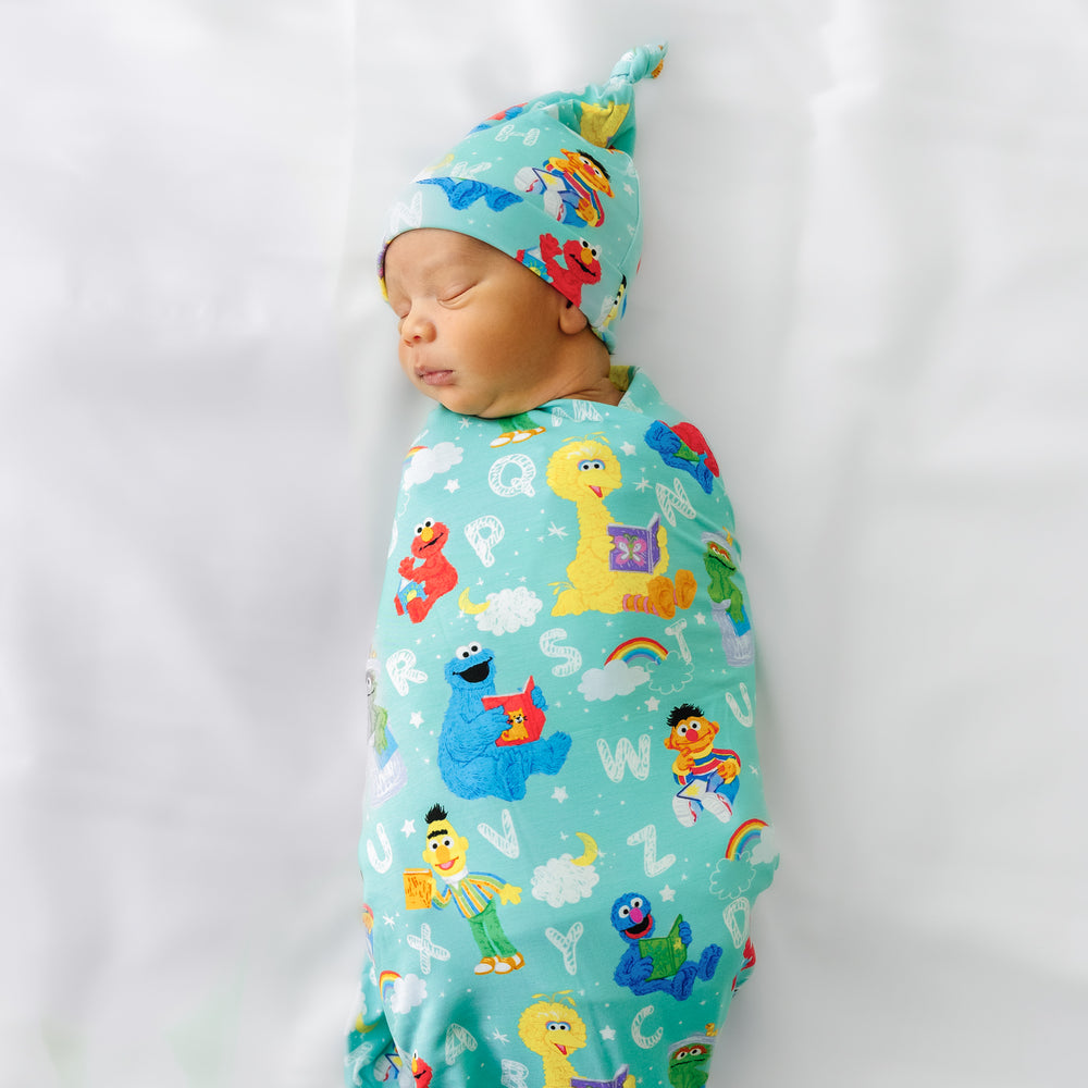 Child laying on a bed swaddled in a Spelling with Sesame Street Swaddle and Hat Set