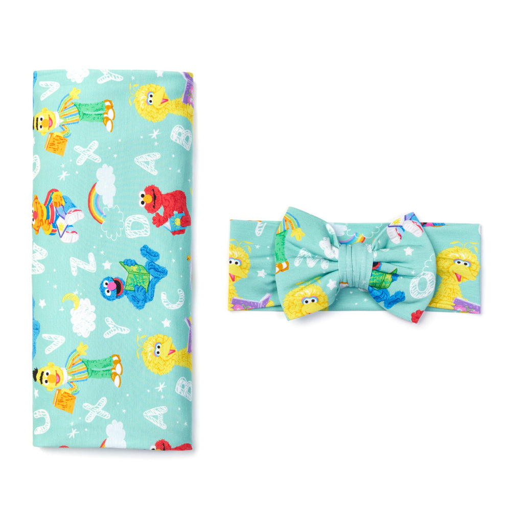 Flat lay image of a Spelling with Sesame Street Swaddle and Luxe Bow Headband set