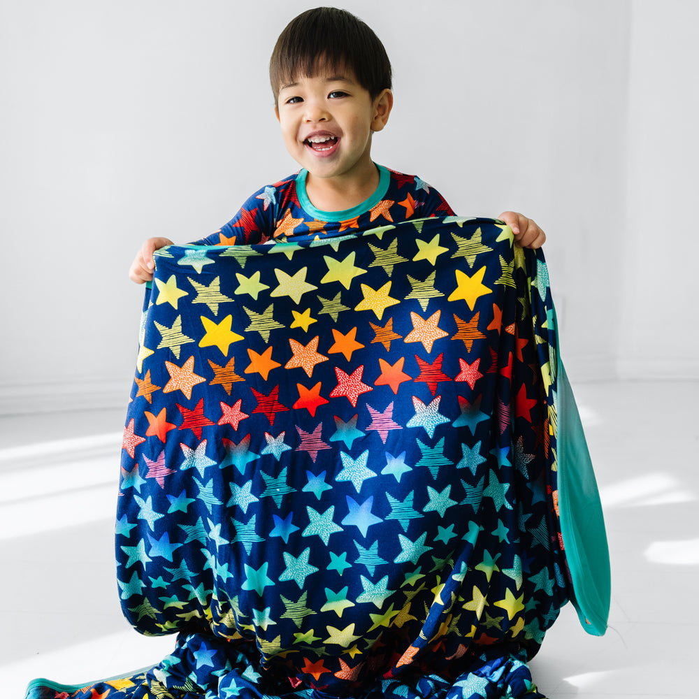 Click to see full screen - Child holding up a Shades of Stars large cloud blanket paired with a matching two piece pajama set
