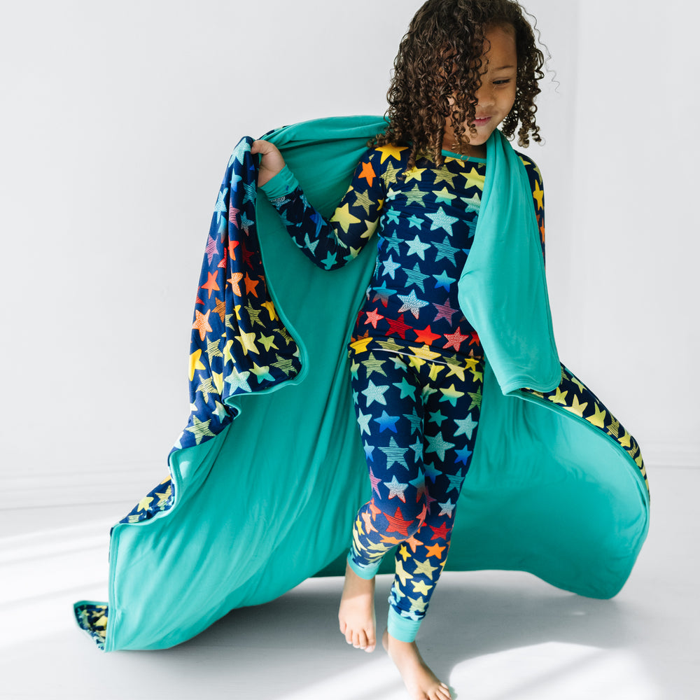 Click to see full screen - Child wearing a Shades of Stars two piece pajama set with a matching large cloud blanket over her shoulders showing the Teal blanket backing