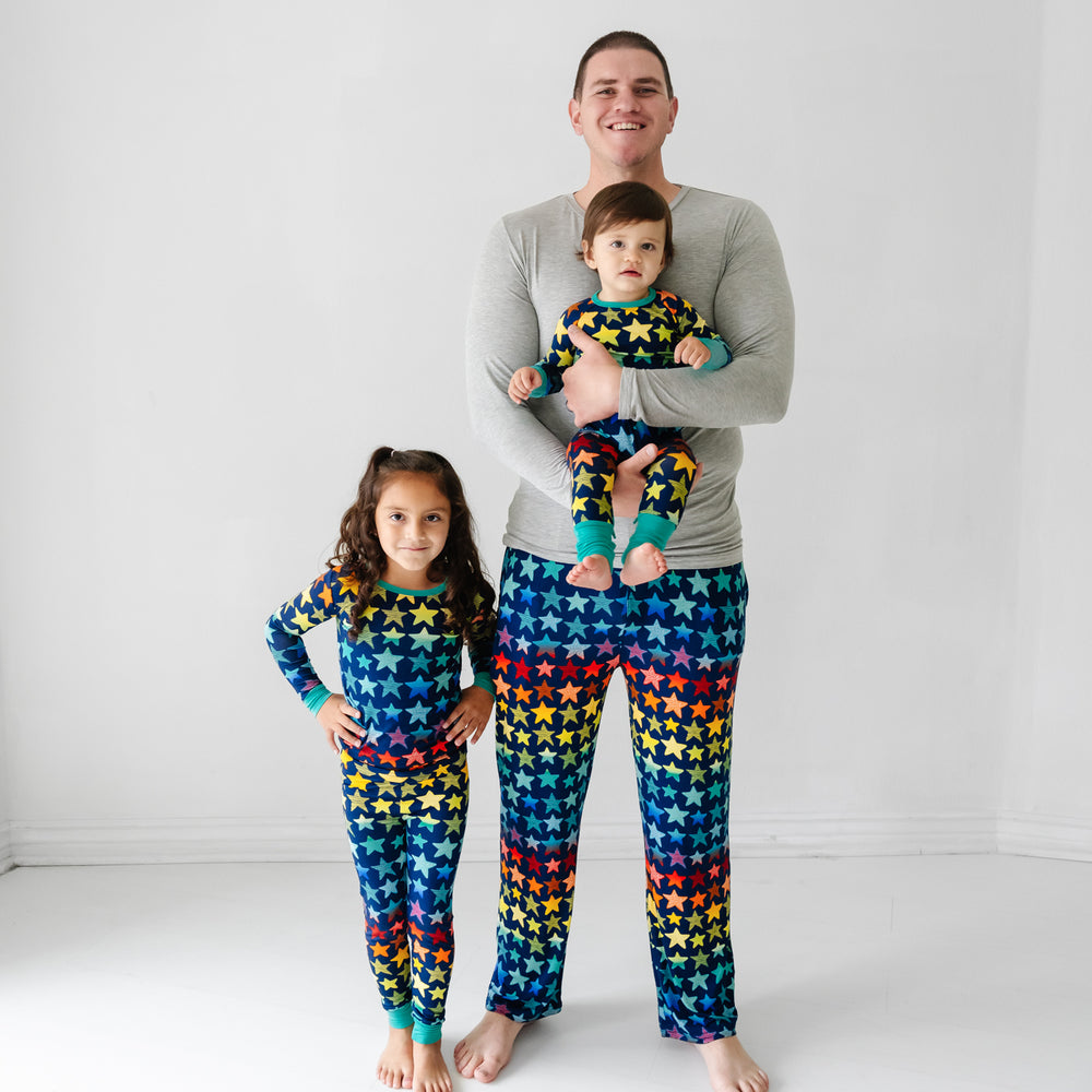 Click to see full screen - Father and his two children matching wearing Shades of Stars pajamas. Dad is wearing Shades of Stars men's pajama pants paired with a Heather Gray men's pajama top. His children are wearing Shades of Stars two piece and crescent zippy pajamas