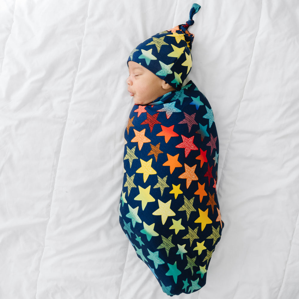 Click to see full screen - Child swaddled in a Shades of Stars swaddle & hat set