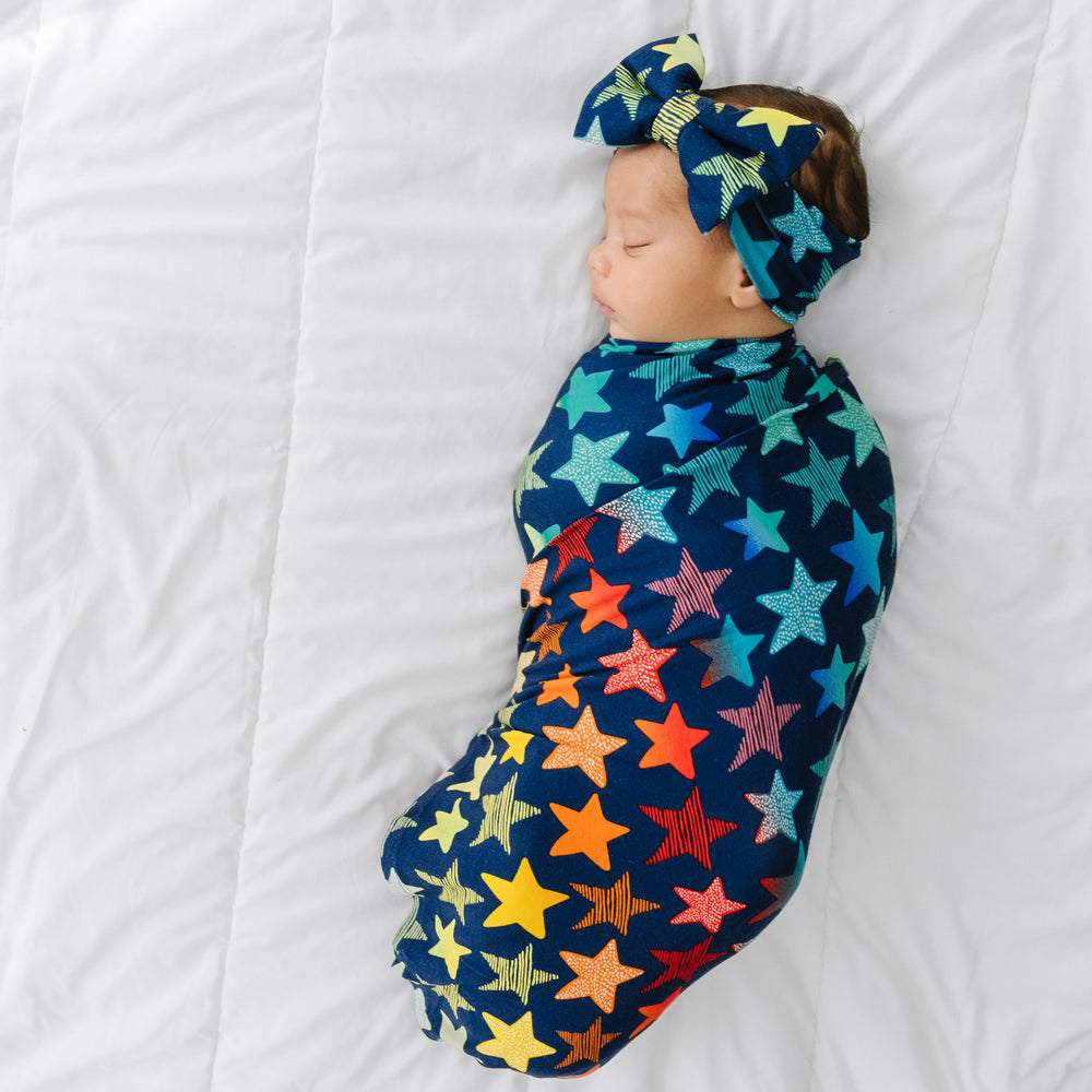 Click to see full screen - Child swaddled in a Shades of Stars swaddle & luxe bow headband set